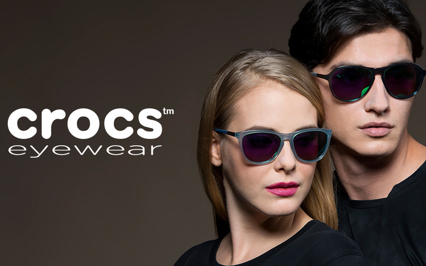A man and a woman are modeling sunglasses for Crocs Eyewear against a dark background.