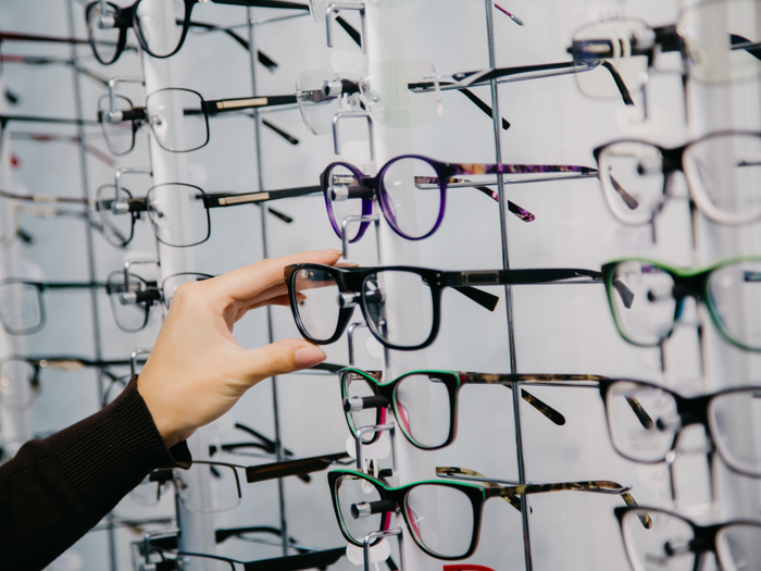 A hand is selecting one pair of glasses from a display of various styles of eyewear.
